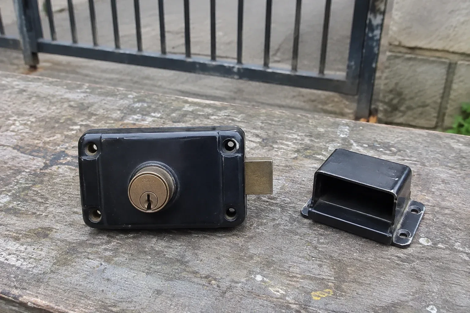 Detached rim gate lock and separate box keeper on an outdoor workbench. — Gate & Building Entry Locks, Burlington