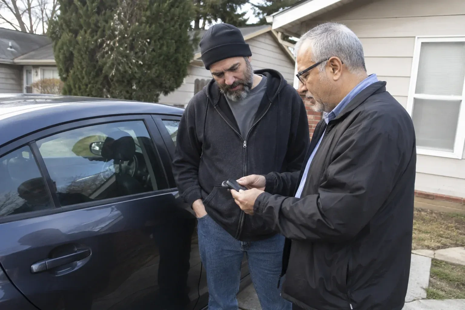 Two adults discussing a key fob beside a parked car. — Car Lockout Service, Burlington
